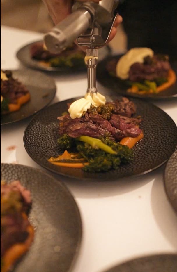 Chef finishing a beef course with kale and carrot purée at the table